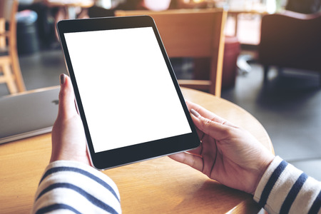 Mockup image of woman's hands holding black tablet pc with blank white desktop screen in cafeの写真素材