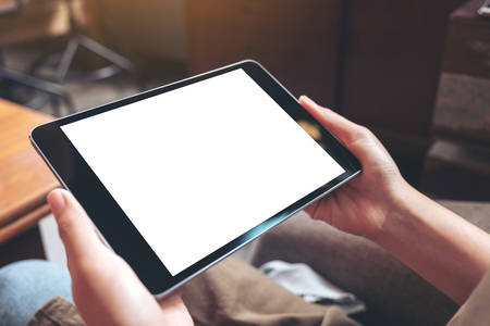 Mockup image of woman's hands holding black tablet pc with blank white desktop screen while sitting in cafeの写真素材