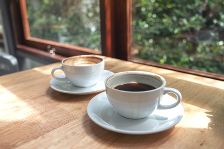 Closeup image of two white cups of hot coffee on wooden table in cafeの写真素材