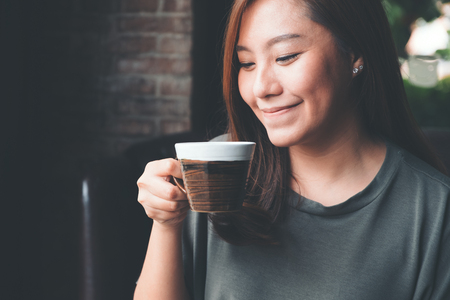 Closeup image of an Asian woman holding and drinking hot coffee with feeling good in vintage cafeの写真素材