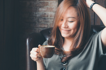Closeup image of a beautiful Asian woman holding and drinking hot coffee with feeling good in vintage cafeの写真素材