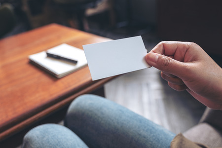 A hand holding white empty business card with notebook on wooden tableの写真素材