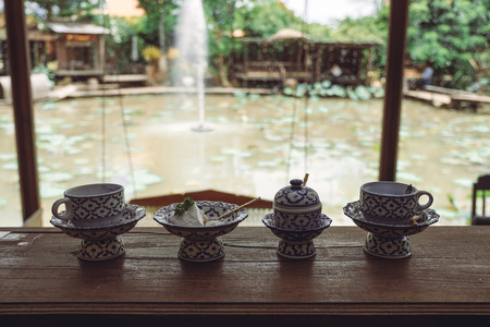 A cup of hot milk with a piece of cake in an antique Thai traditional benjarong style containers with nature backgroundの写真素材