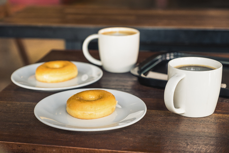 Two set of donuts in a white plate with coffee cups on wooden tableの写真素材