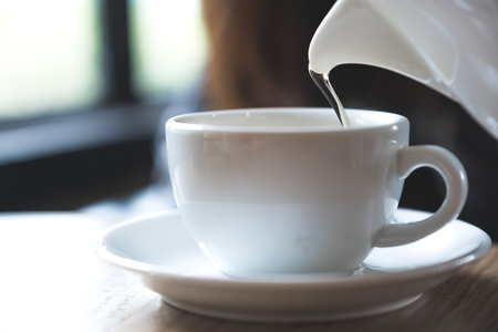 Closeup image of a person holding teapot and pouring tea into a white cup on wooden tableの写真素材