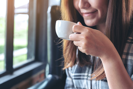 Closeup image of an asian woman holding and drinking hot coffee with feeling good in cafeの写真素材