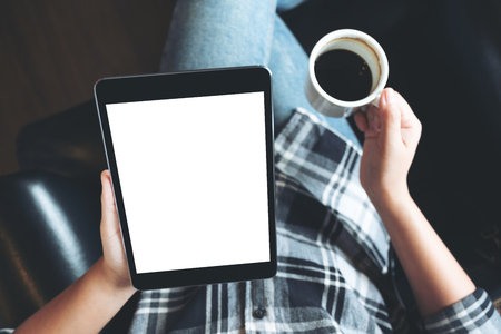 Top view mockup image of a woman sitting cross legged and holding black tablet pc with blank white desktop screen in cafeの写真素材