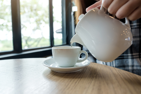 A hand holding teapot and pouring tea into a white cup on wooden tableの写真素材