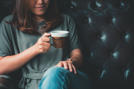Closeup image of a beautiful Asian woman holding and drinking hot coffee with feeling good in vintage cafeの写真素材