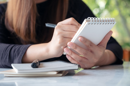 A woman holding and writing on notebook while sitting in cafe with blur green nature backgroundの写真素材