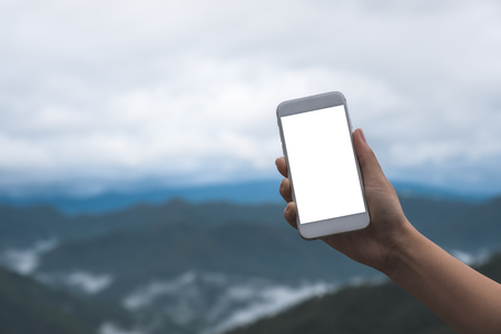 Mockup image of a hand holding and showing white smart phone with blank desktop screen in outdoor with blur green mountains backgroundの写真素材