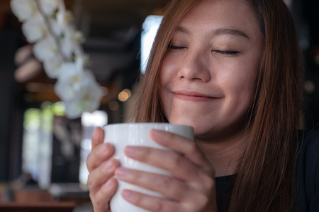 Closeup image of Asian woman close her eyes to smelling and drinking hot coffee with feeling good in cafeの写真素材