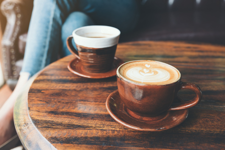 Closeup image of two cups of hot latte coffee and black coffee on vintage wooden table in cafeの写真素材