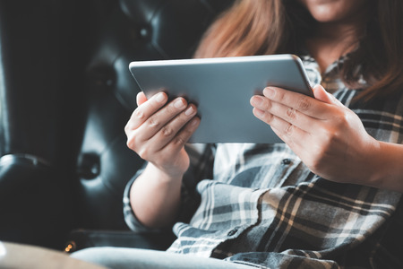 Closeup image of a woman holding and using tablet pc in modern cafe