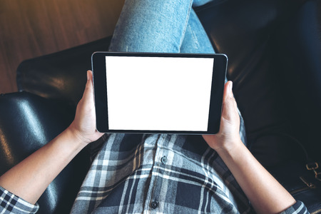 Top view mockup image of a woman sitting cross legged and holding black tablet pc with blank white...