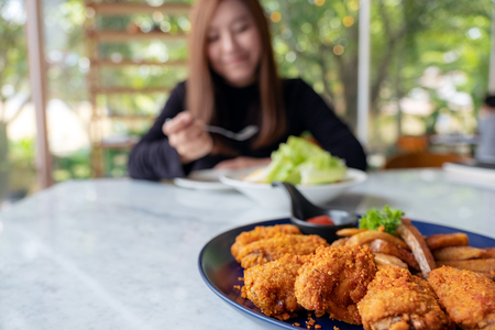 Closeup image of a plate of fried chicken and french fries with a woman eating salad in the restaurantの写真素材