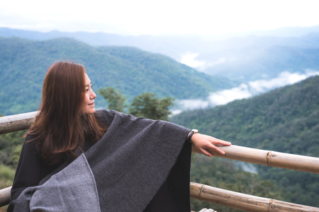 A woman sitting alone and looking at mountains on foggy day with blue sky background in the morningの写真素材
