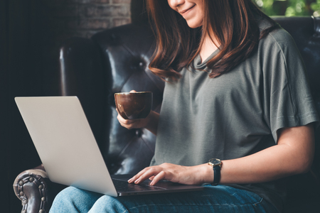 Closeup image of a woman working , using and typing on laptop keyboard while drinking coffeeの写真素材