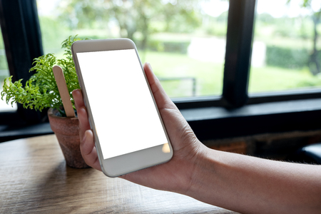 Mockup image of a hand holding a white mobile phone with blank screen on table in the houseの写真素材
