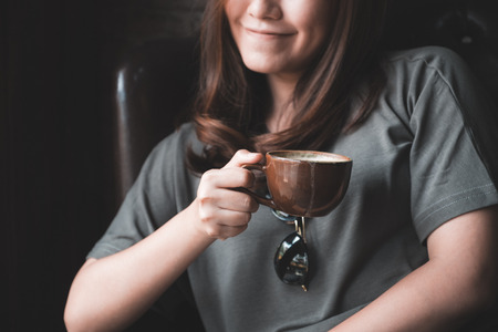 Closeup image of a beautiful Asian woman holding and drinking hot coffee with feeling good in vintage cafeの写真素材