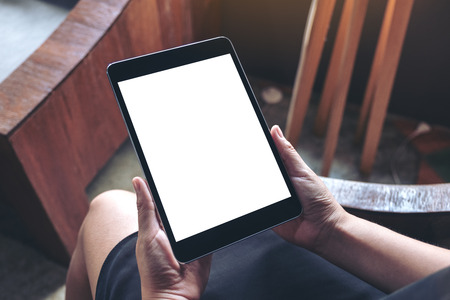 Top view mockup image of a woman sitting and holding black tablet pc with blank white desktop screenの写真素材
