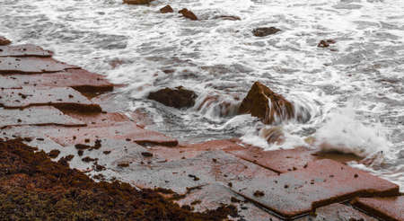 A view of ocean waves hitting the Galveston Seawall on a moss lined stone walkwayの素材