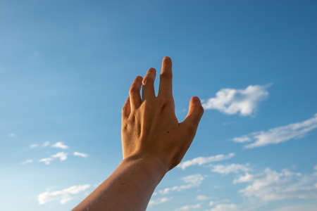 Hand reaching for the sky. Hand on evening blue sky backgroundの写真素材