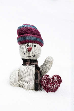 old rag doll in the snow with a red heart on white backgroundの写真素材