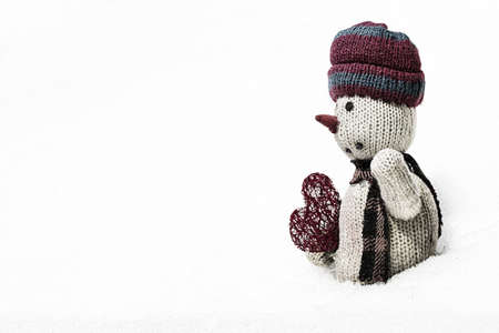 old rag doll in the snow with a red heart on white backgroundの写真素材