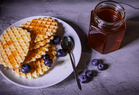 There are fresh pastries and honey on the table, sprinkled with blueberries next to it