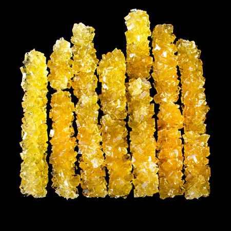A row of yellow sticks with a black background. The sticks are made of sugar and are arranged in a...