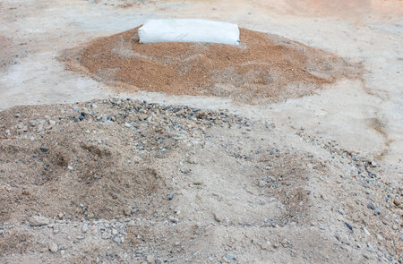 There is construction sand on the ground, and on top of it there is a bag of cement for preparing mortar for laying bricks.の写真素材