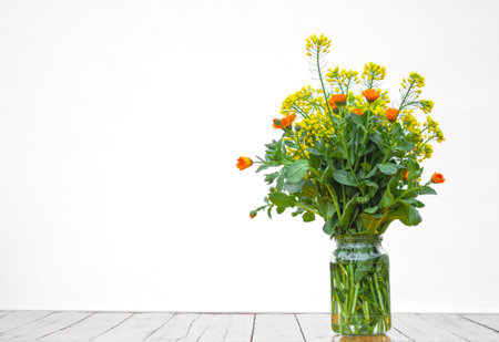 Yellow and orange flowers in glass bowl stand on table against white wall