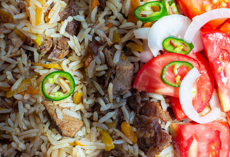 A rice dish with meat, garnished with a salad of chopped tomatoes, onions and hot green chili peppers. The photo is suitable for both the restaurant business and any food related designの写真素材