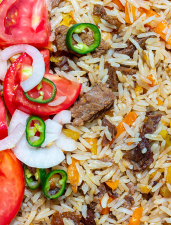 A rice dish with meat, garnished with a salad of chopped tomatoes, onions and hot green chili peppers. The photo is suitable for both the restaurant business and any food related designの写真素材