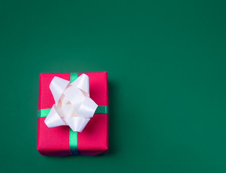 Christmas gift in a red box with white bows on a green background, with empty space for textの写真素材