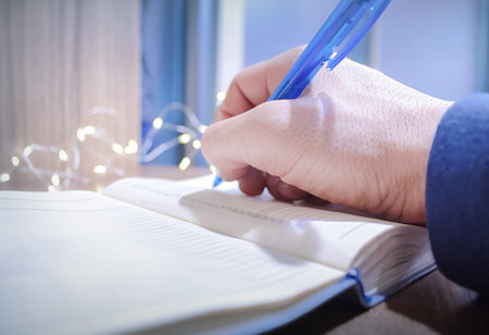A man writes down his plans and goals for the New Year in a notebook, while small garlands sparkle nearbyの写真素材