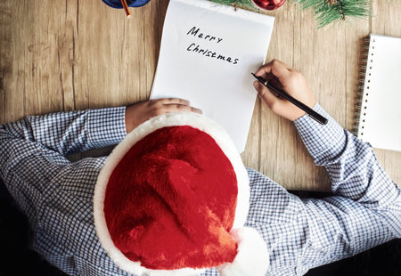 A guy in a Santa hat writes Merry Christmas on a white piece of paperの写真素材