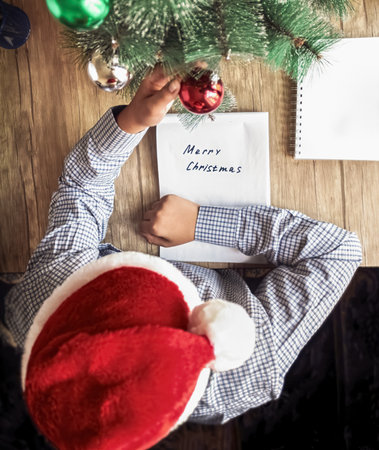 A guy in a Santa Claus hat holds a Christmas tree decorationの写真素材