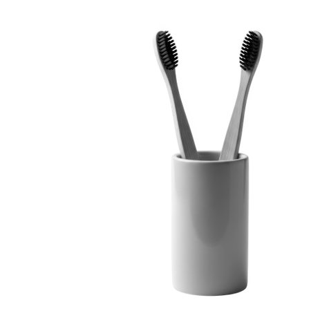 A close-up studio shot of two natural bamboo toothbrushes with black bristles, elegantly held upright in a simple gray ceramic holder, showcasing eco-friendly oral care.の素材