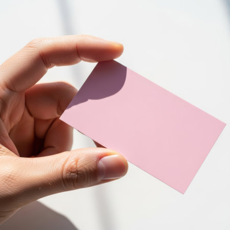 A person's hand delicately holds a blank pink card, ready for personalization. This image evokes concepts of branding, marketing, identity, and professional presentation in a clean, modern style.の素材