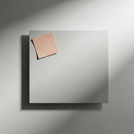 A square mirror with a subtle reflection displays a small, soft pink paper note attached to its upper left corner. The scene is lit softly, creating a clean and minimalist aesthetic.の素材
