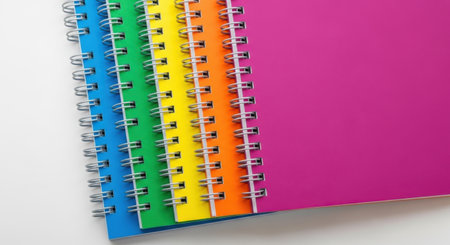 A vibrant stack of spiral-bound notebooks in rainbow colors, presented isolated on a clean white background.の素材