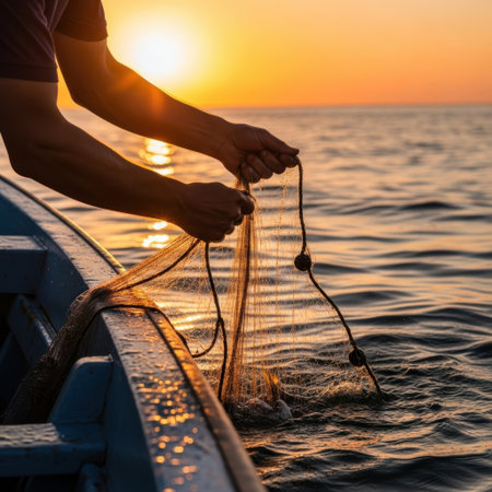 Close-up of a fisherman's hands as they meticulously prepare a fishing net on a boat. The warm glow of a spectacular sunset illuminates the water, creating a serene and picturesque scene.の素材