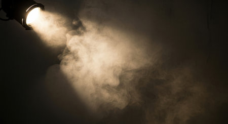 A powerful spotlight beam cuts through darkness, revealing a dense cloud of swirling smoke.の素材