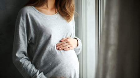 Pregnant woman holding her belly by a window