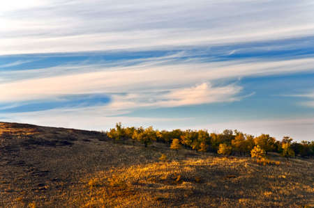 The sun illuminates the hill and colorful autumn leavesの写真素材