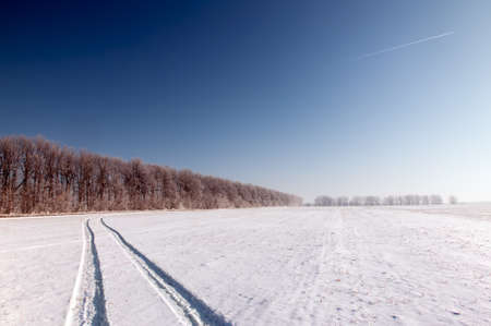 Landscape with a trace of the aircraft in the clear sky and a long snowy country roadの写真素材