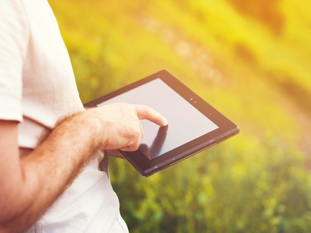 Smart casual man with digital tablet outdoors, close up. Focus on finger. Sunkissed effect with...