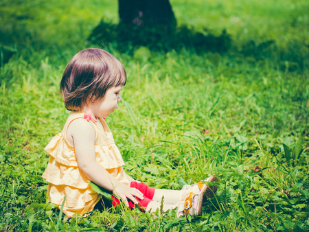 One year old baby girl sitting on grass and looking away. Colorful image with copy spaceの写真素材